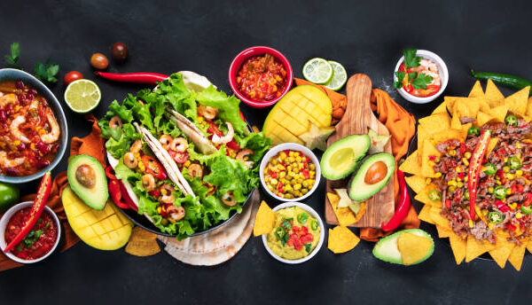 Mexican meal board with nachos, tacos, guacamole, shrimps, avocado and starfruit. Hot and spicy